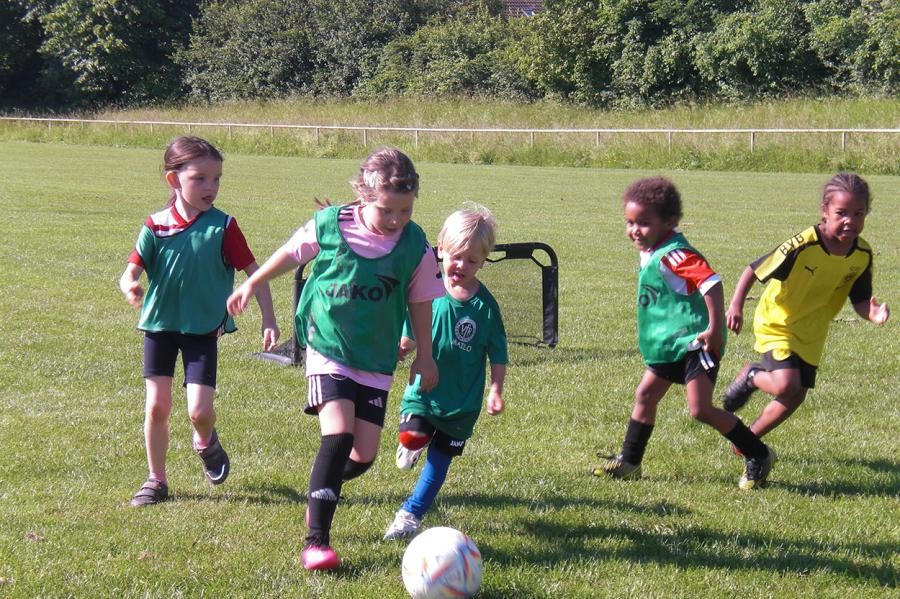 Einige kleine Kinder in Fußballtrikots rennen einem Ball nach.