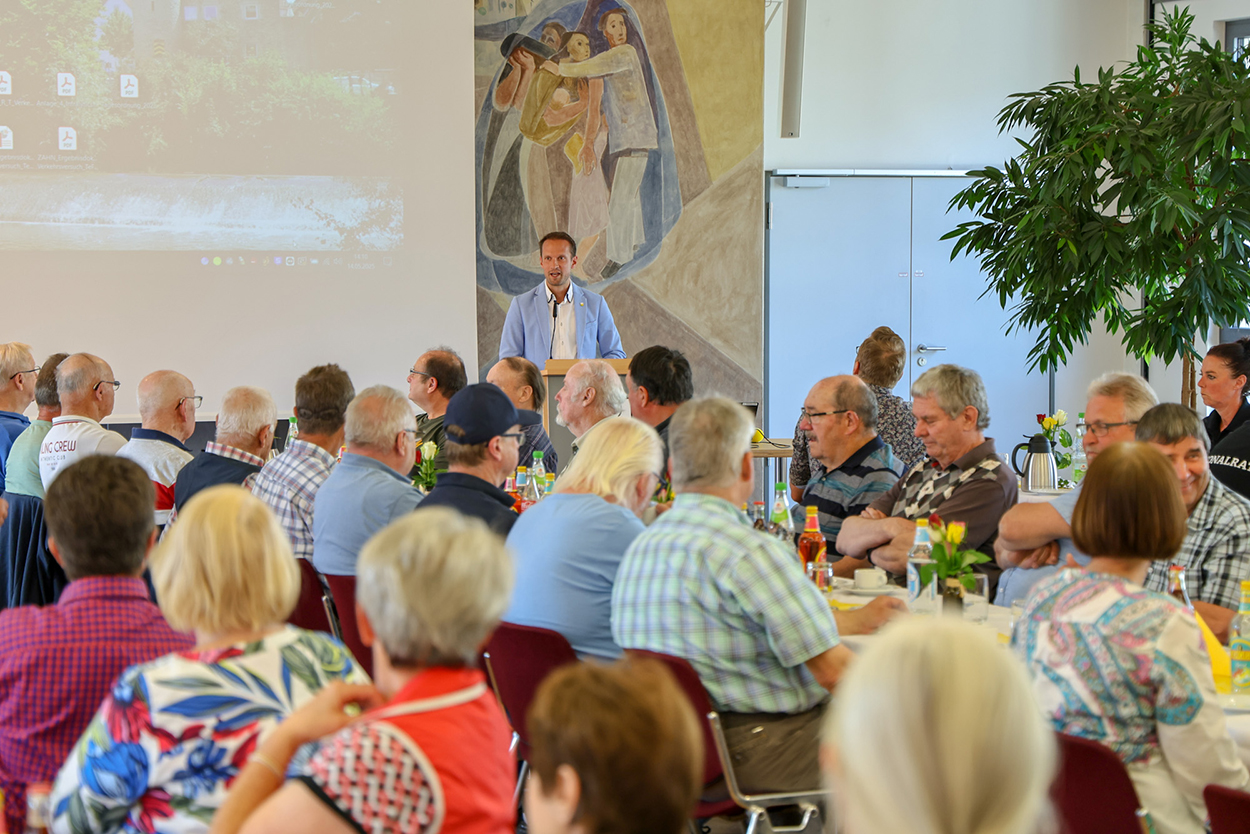 Stadtverwaltung Ein Mann im Hintergrund am Rednerpult, davor viele Zuhörende an Tischen