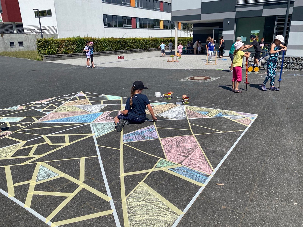 Ein Kind sitzt in einer Kreidemalerei auf der Straße, andere Kinder spielen