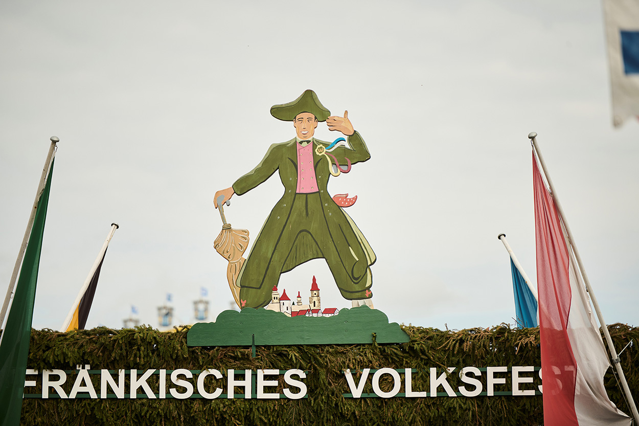 Eine Holzfigur auf einem Torbogen mit er Aufschrift "Fränkisches Volksfest"