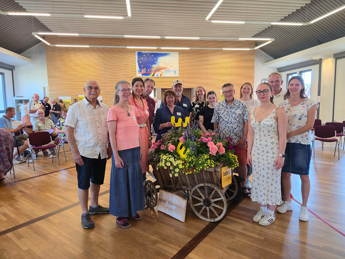 Eine Gruppe steht um einen kleinen Wagne mit Blumen und lächelt in die Kamera