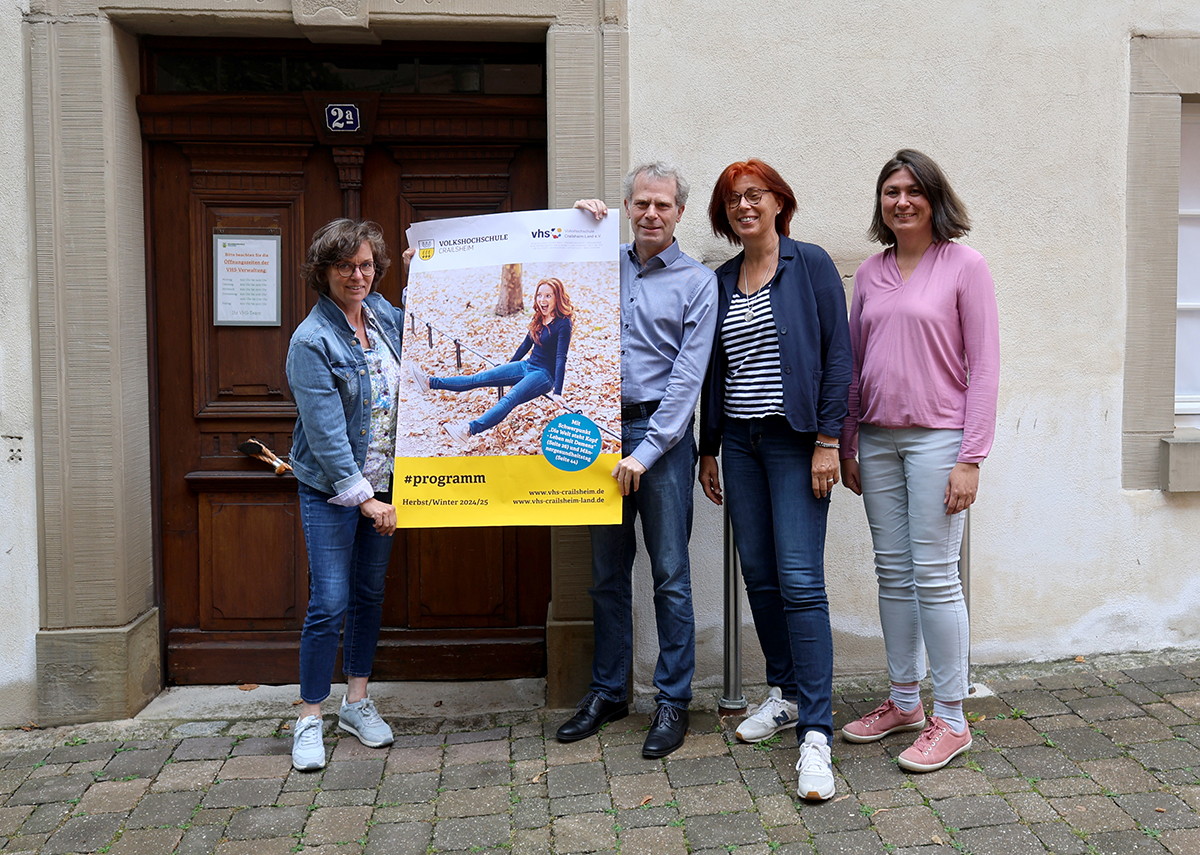 Drei Frauen und ein Mann präsentieren ein Programm-Plakat.