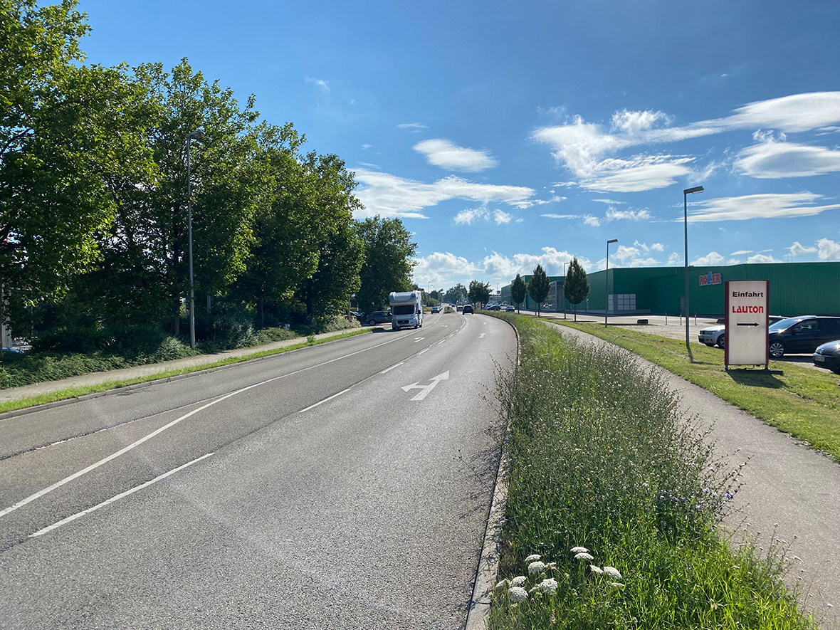 Eine Straße mit eingen Fahrbahnschäden bei Sonnenschein.