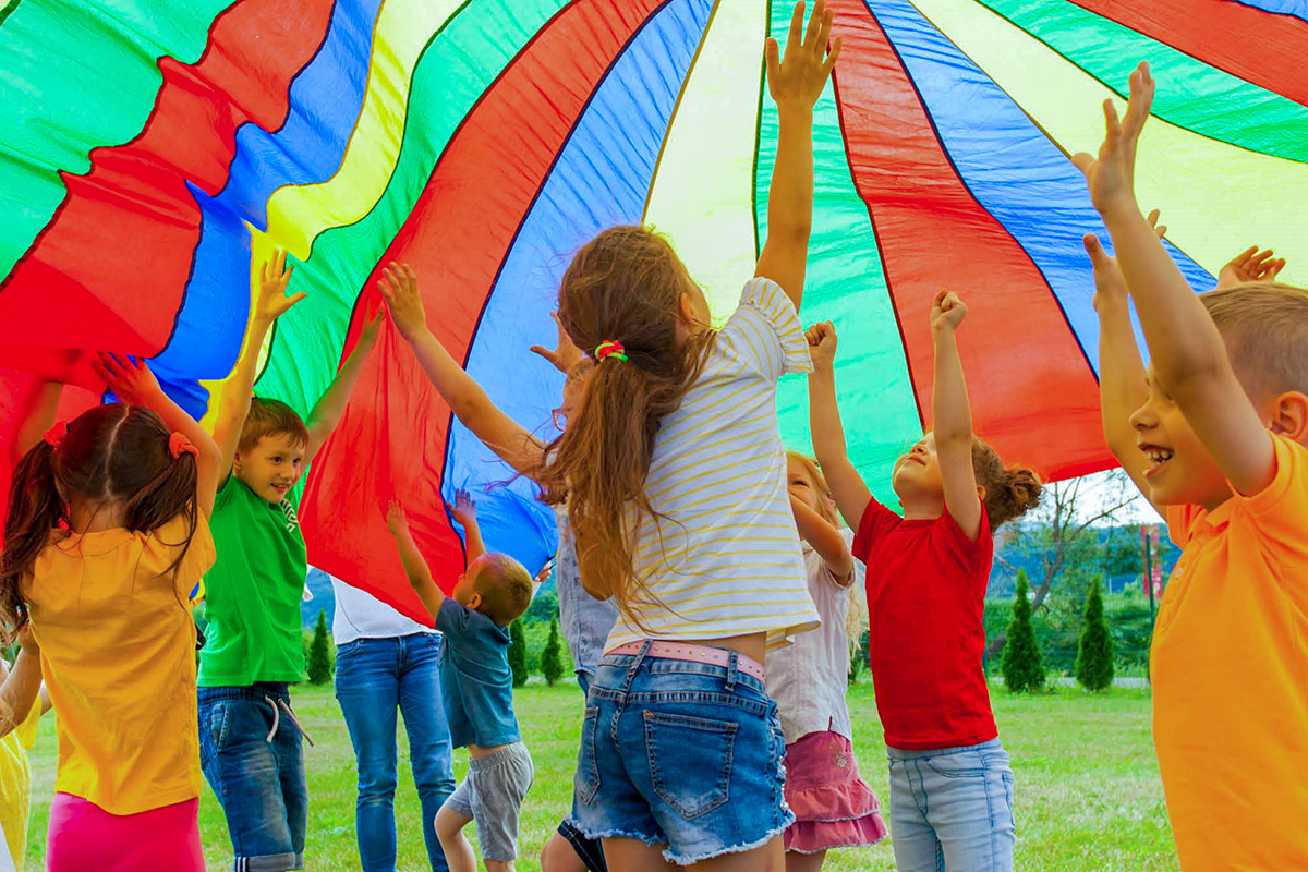 spielende Kinder unter einem aufgeblähten bunten Fallschirm