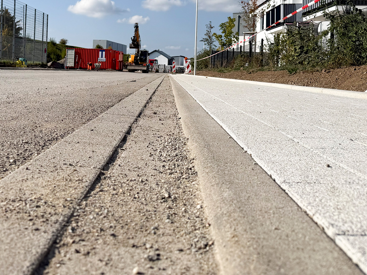 ein neu gemachter Gehweg, eine Straße, weit im Hintergrund Baugeräte